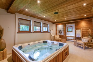 A spa room with a hot tub, wooden ceiling, and two windows with blinds.