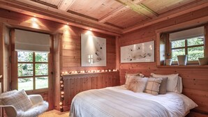 Een houten slaapkamer met een groot bed, een schommelstoel en een raam met uitzicht op groen.