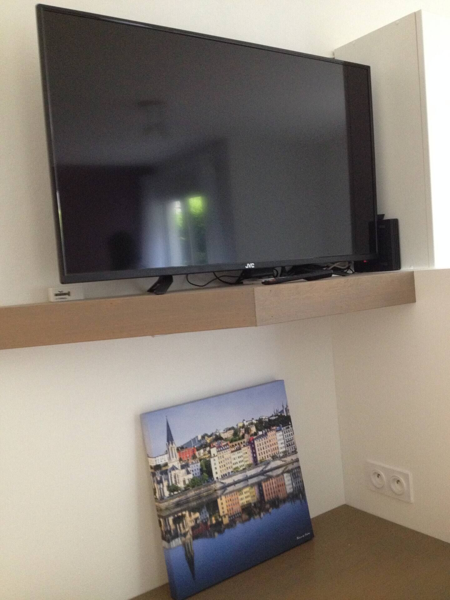 Un téléviseur à écran plat fixé sur une étagère en bois, au-dessus d’un tableau représentant une vue urbaine.