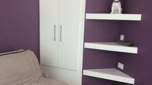 Una habitación con sofá color beige, armario blanco y paredes moradas con estantes blancos.