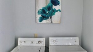 Dos lavadoras de carga frontal blancas en un cuarto de lavado con una pared gris y un cuadro de flores azules encima.