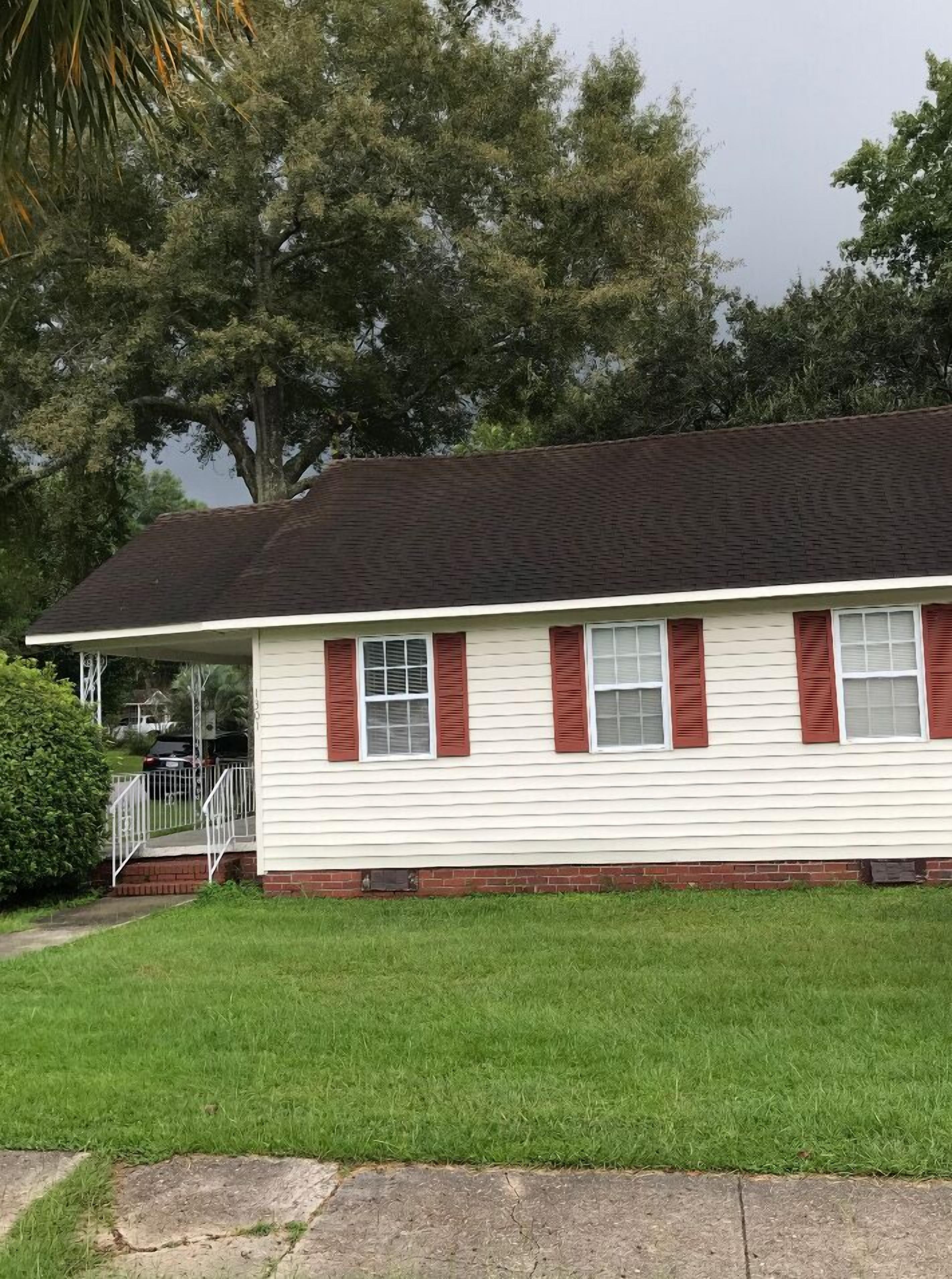 A single-story house with a dark roof, white siding, and red shutters.