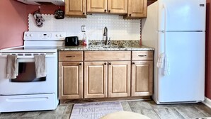Una cocina compacta con armarios de madera, un refrigerador blanco, una estufa y un lavamanos.