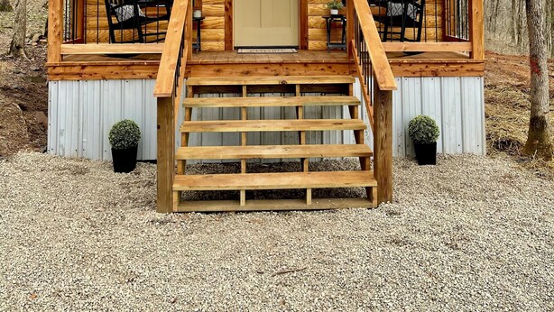 A wooden cabin with a front porch, two windows, and a door.