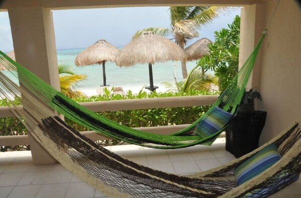 Een hangmat op een balkon met uitzicht op het strand en rieten parasols.