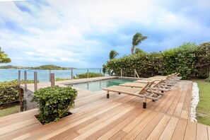 A wooden deck with lounge chairs overlooking a pool and ocean view.