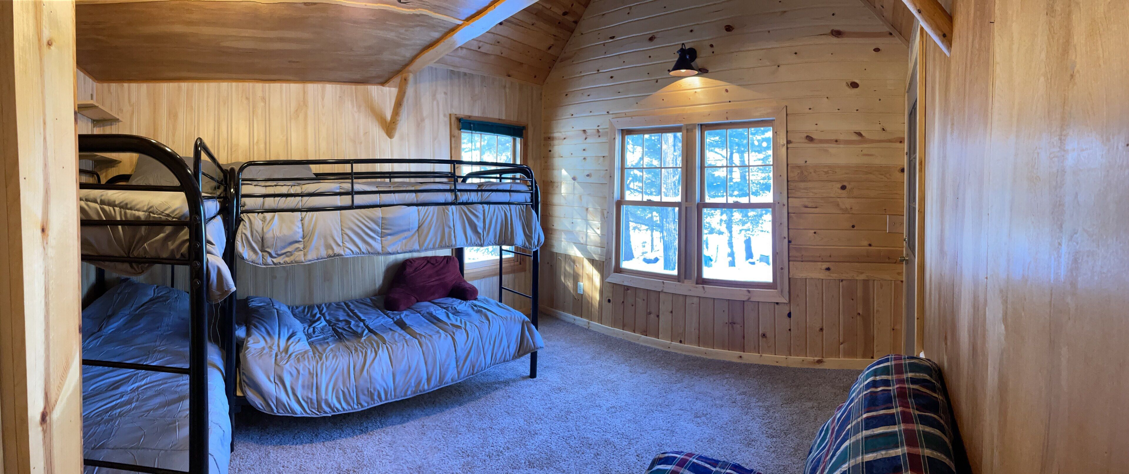 Une pièce de cabane en bois avec des lits superposés, une fenêtre et une couverture à carreaux sur le sol.