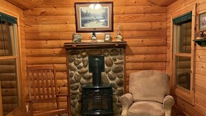 Interior acogedor de una cabaña de madera con chimenea de piedra, una mecedora y un sillón mullido.