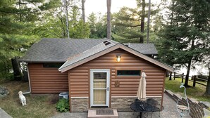 Una cabaña de troncos con base de piedra, una puerta de madera y un pequeño patio con mesa y sillas.