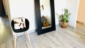 Een moderne kamer met een spiegel met donkere rand, een zwarte stoel met een kussen in wit en bruin, en een cactus in een houten pot.