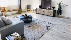 Een moderne woonkamer met een bank, salontafel, televisie en een potplant.