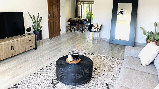 Een moderne woonkamer met een flatscreen televisie, een rond zwart voetenbankje, een grijze bank en een plafondventilator.
