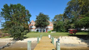 A wooden pier leading to a brick building with a balcony, surrounded by trees and a sandy beach. - Beautiful, spacious waterfront home, an easy walk to historic Chestertown (Chestertown)