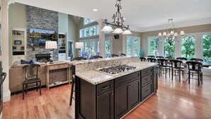 A spacious kitchen with a large island, dark cabinetry, and a stone accent wall. - Foreststone Fabulous Lake Keowee Waterfront Home (West Union)