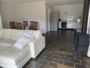 Een ruime woonkamer met een grote witte leren bank, een open haard en een keuken op de achtergrond.