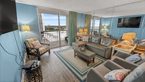A spacious living room with a sofa, armchairs, and a coffee table. A balcony with a railing is visible through the glass doors. - S Hampton 704 2 Br Oceanview in Kingston, Pool (Myrtle Beach)