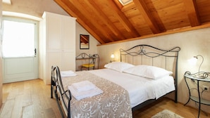 A bedroom with a wooden ceiling, a bed with white linens, a bedside table with a lamp, and a chair. - Heritage Family Apartment Mama 3 in Omiš, free parking (Omiš)