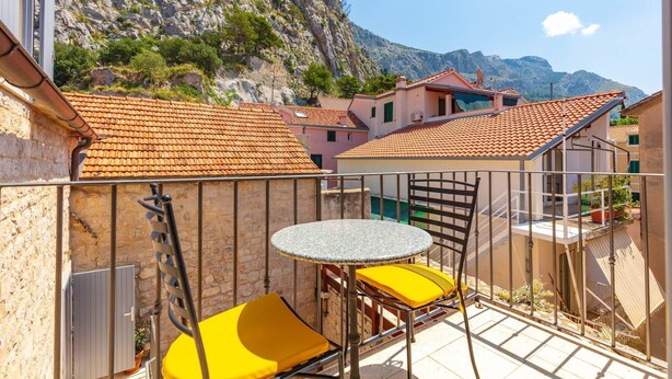 A balcony with a round table and two yellow chairs, overlooking a mountainous landscape with terracotta-roofed buildings. - Heritage Family Apartment Mama 3 in Omiš, free parking (Omiš)