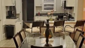Comedor con mesa y sillas de vidrio, ventilador de techo y armarios blancos.