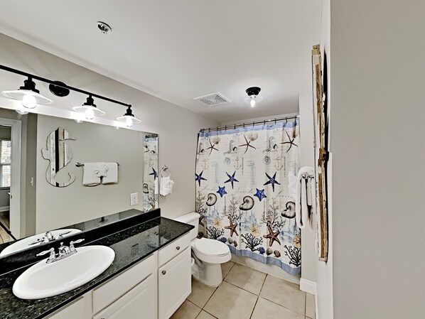 A bathroom with a white sink, black countertop, and a shower curtain with nautical designs.