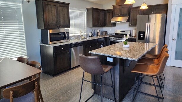 A modern kitchen with dark wood cabinets, stainless steel appliances, and a central island with bar stools. - South Salem - Close to I-5 and Costco, easy Shop and Eat (Salem)
