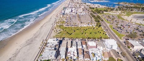 Vue aérienne d’une zone côtière avec une plage, des parkings et des bâtiments.