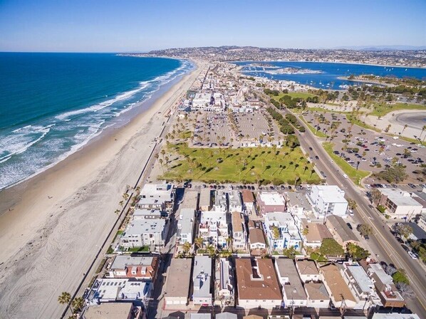 Vista aérea de una zona costera con playa, estacionamientos y edificios.