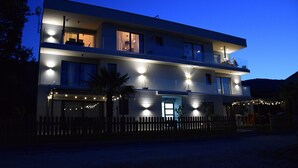A modern two-story building with illuminated windows and a balcony, surrounded by a wooden fence. - 2 Bed House - Sleeps 4 - Hottub - Garden - Parking (Rasa)