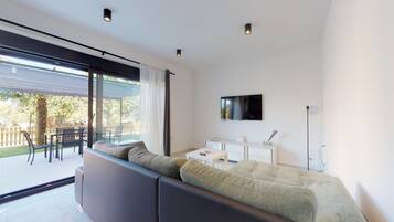 A modern living room with a large sectional sofa, a flat-screen TV mounted on the wall, and a dining area with a table and chairs.