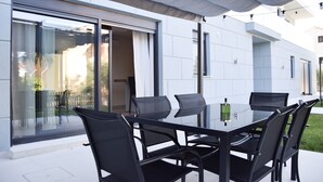 A modern outdoor dining area with a glass table and black chairs, adjacent to a white building with large sliding glass doors. - 2 Bed House - Sleeps 4 - Hottub - Garden - Parking (Rasa)