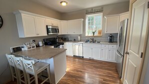 Une cuisine avec des meubles blancs, un îlot central doté de chaises, un four à micro-ondes, une cuisinière, un évier et un réfrigérateur.