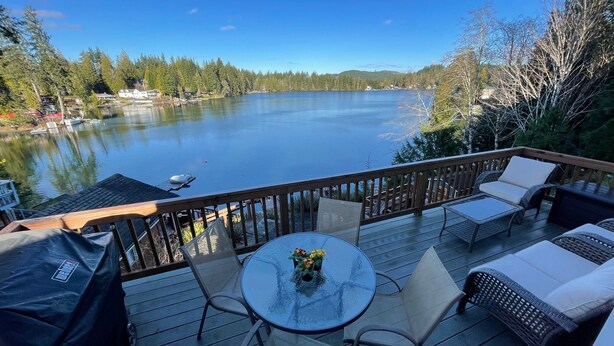 Une terrasse dotée de mobilier d’extérieur, offrant une vue sur un lac et entourée d’arbres.