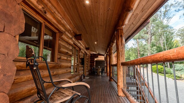 A wooden log cabin with a porch, wooden benches, and a railing.