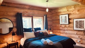 A cozy log cabin bedroom with a bed, bedside lamps, a mirror, and framed pictures on the walls.