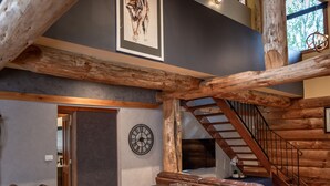 A spacious living area with a wooden staircase, a fireplace, and a large chandelier.