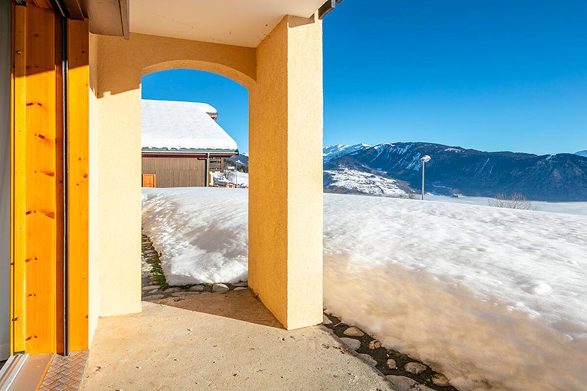 Un paisaje nevado con una montaña al fondo y un edificio con techo cubierto de nieve.