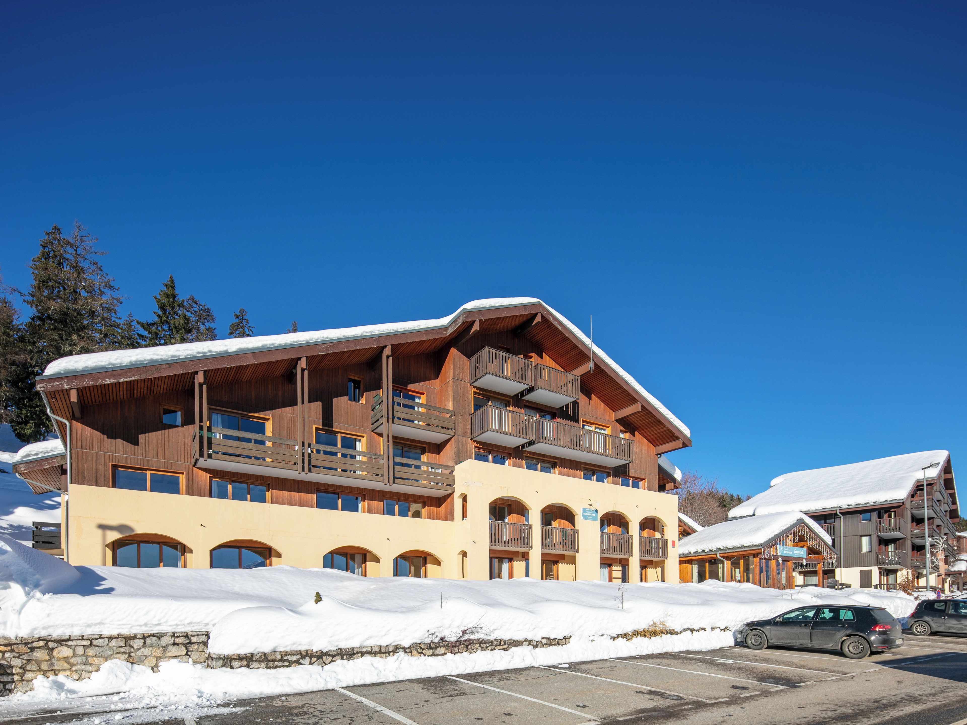Un hôtel à plusieurs étages, doté de balcons en bois, avec des pistes de ski en arrière-plan.