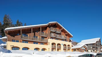 Un hôtel à plusieurs étages, doté de balcons en bois, avec des pistes de ski en arrière-plan.