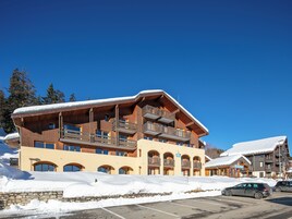 Ein mehrstöckiges Hotel mit hölzernen Balkonen und Skipisten im Hintergrund.