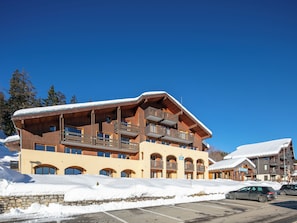 A multi-story hotel with wooden balconies and ski slopes in the background. - Residence Le Beauregard - Vacanceole (La Léchère)