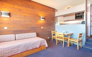 Una habitación con pared de madera, un sofá, una mesa con sillas y una zona de kitchenette.