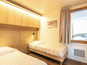 A bedroom with a bed, a headboard, a wall-mounted light, a window with curtains, and a wall-mounted air conditioning unit. - Residence Le Beauregard - Vacanceole (La Léchère)