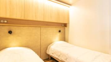 Een kamer met twee éénpersoonsbedden, houten hoofdborden en een lichtgekleurde muur.