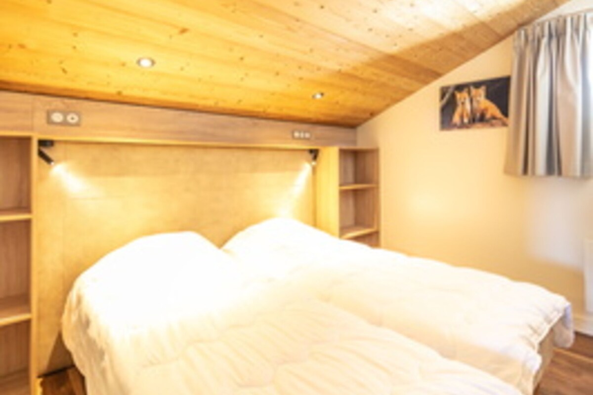 A room with a wooden ceiling, a bed with white bedding, and a small shelf unit.