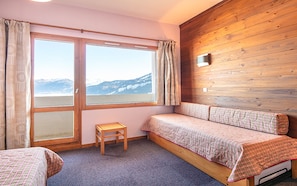 Una habitación con dos camas, una mesita y una ventana con vistas a las montañas.