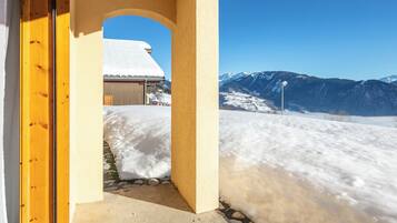 A snow-covered landscape with a mountain view, a building with a snow-covered roof, and a clear blue sky.