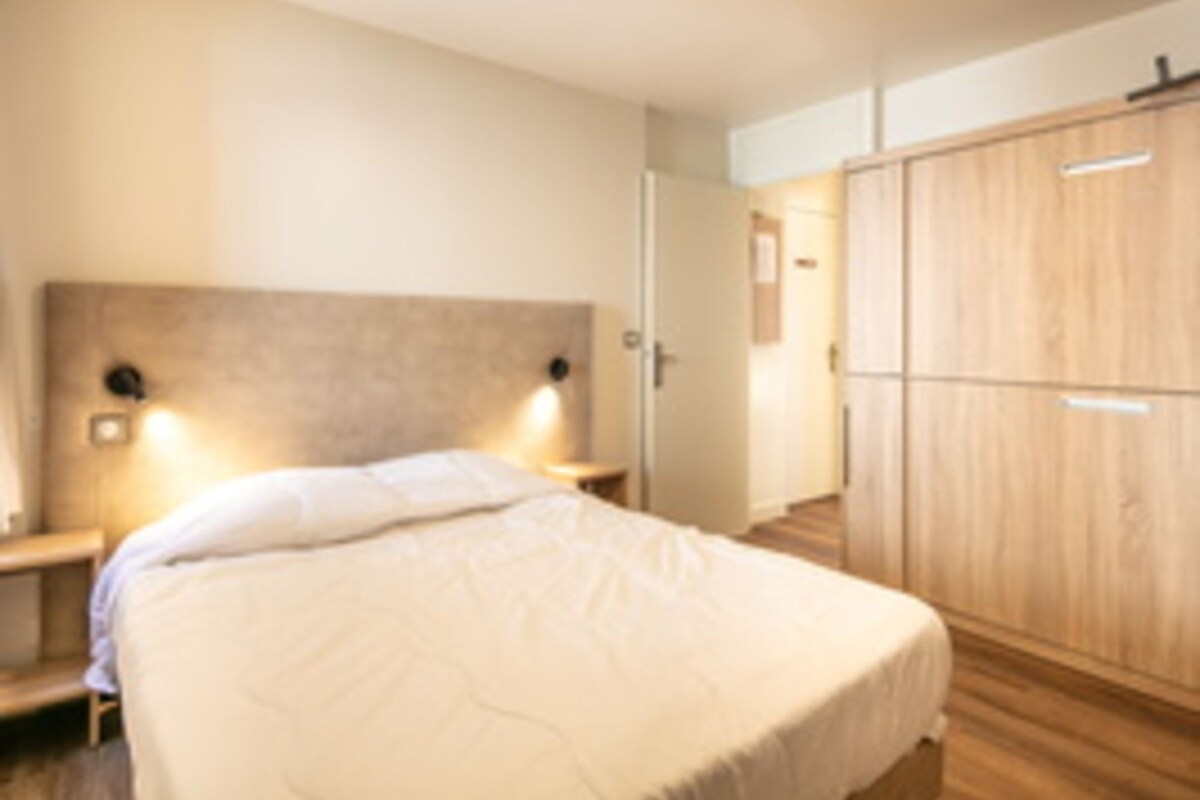 A bedroom with a bed, bedside tables, a wardrobe, and wall-mounted lights.