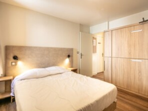 A bedroom with a bed, bedside tables, a wardrobe, and wall-mounted lights. - Residence Le Beauregard - Vacanceole (La Léchère)