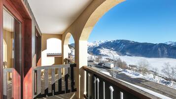 Un balcon avec vue sur des montagnes enneigées et une route où circulent des véhicules.