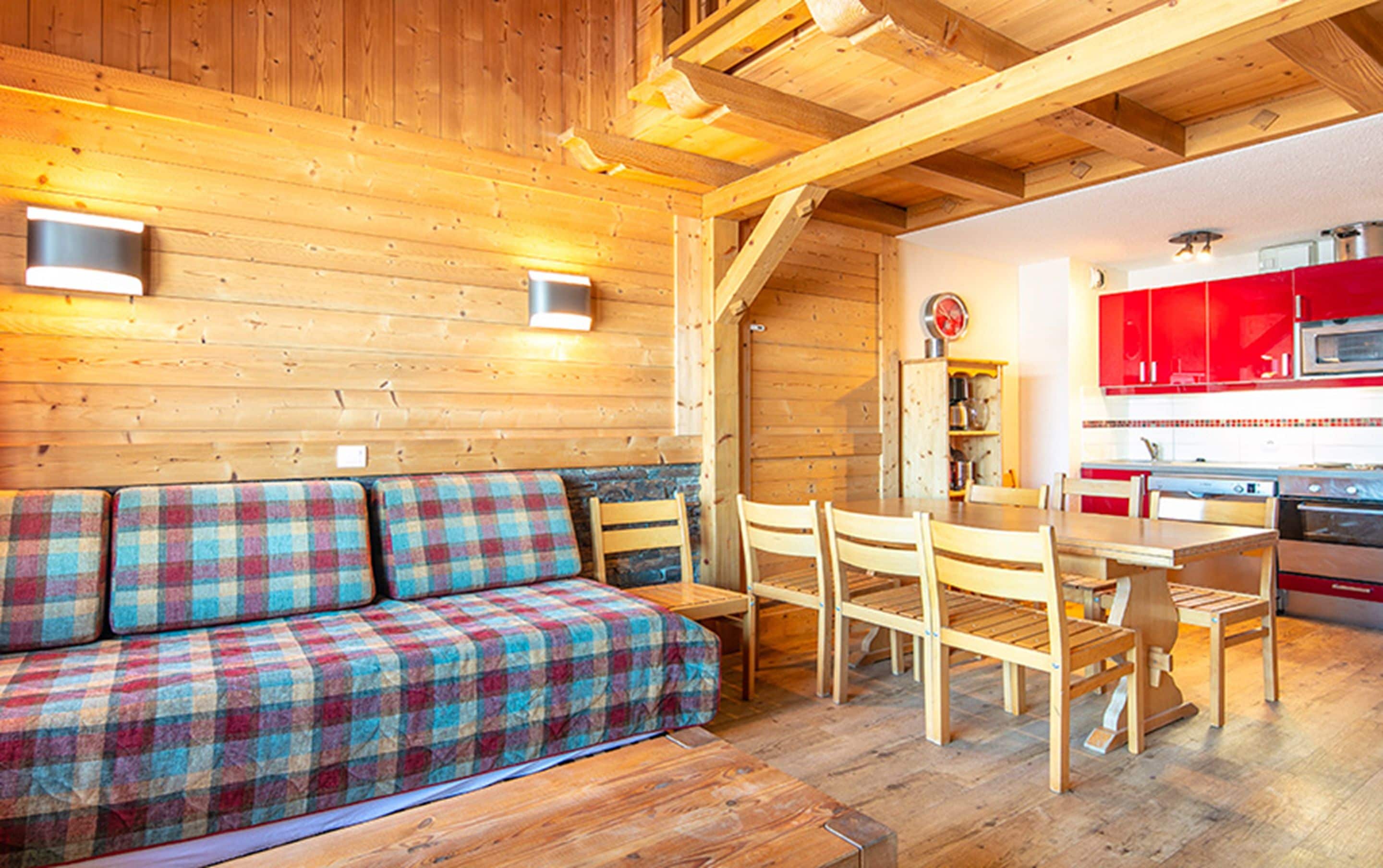 Un interior de madera con sofá, mesa de comedor, sillas y una zona de cocina con armarios rojos.